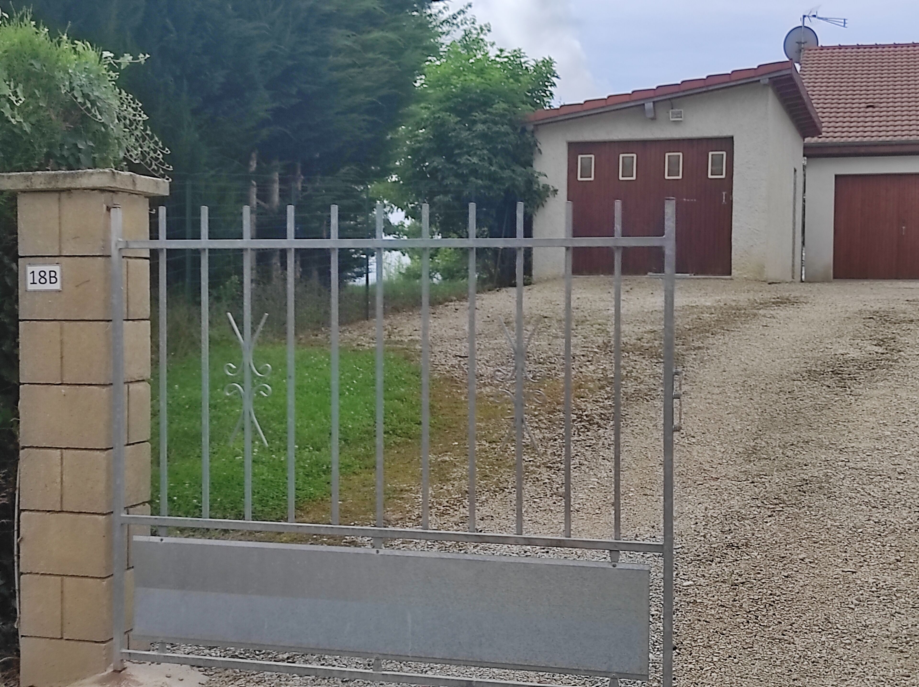 Une propriétéClose, avec une allée en gravier menant à un bâtiment doté d’un toit rouge et d’un garage.