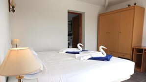 A neatly made bed with white linens and two swan-shaped towels, a wooden wardrobe, and a lamp on a bedside table. - La Novela - Calpe, Costa Blanca (Calpe)