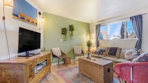 Ein Wohnzimmer mit Fernseher, Korbmöbeln, einer Couch und einem Fenster mit Vorhängen.