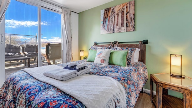 Ein Hotelzimmer mit einem großen Bett, Bergblick, einem Bild an der Wand und einem kleinen Tisch mit einer Lampe.
