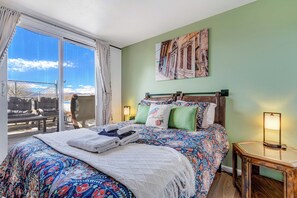 A hotel room with a large bed, a view of mountains, a painting on the wall, and a small table with a lamp. - 180° Mountain Range Views and Centrally Located (Colorado Springs)