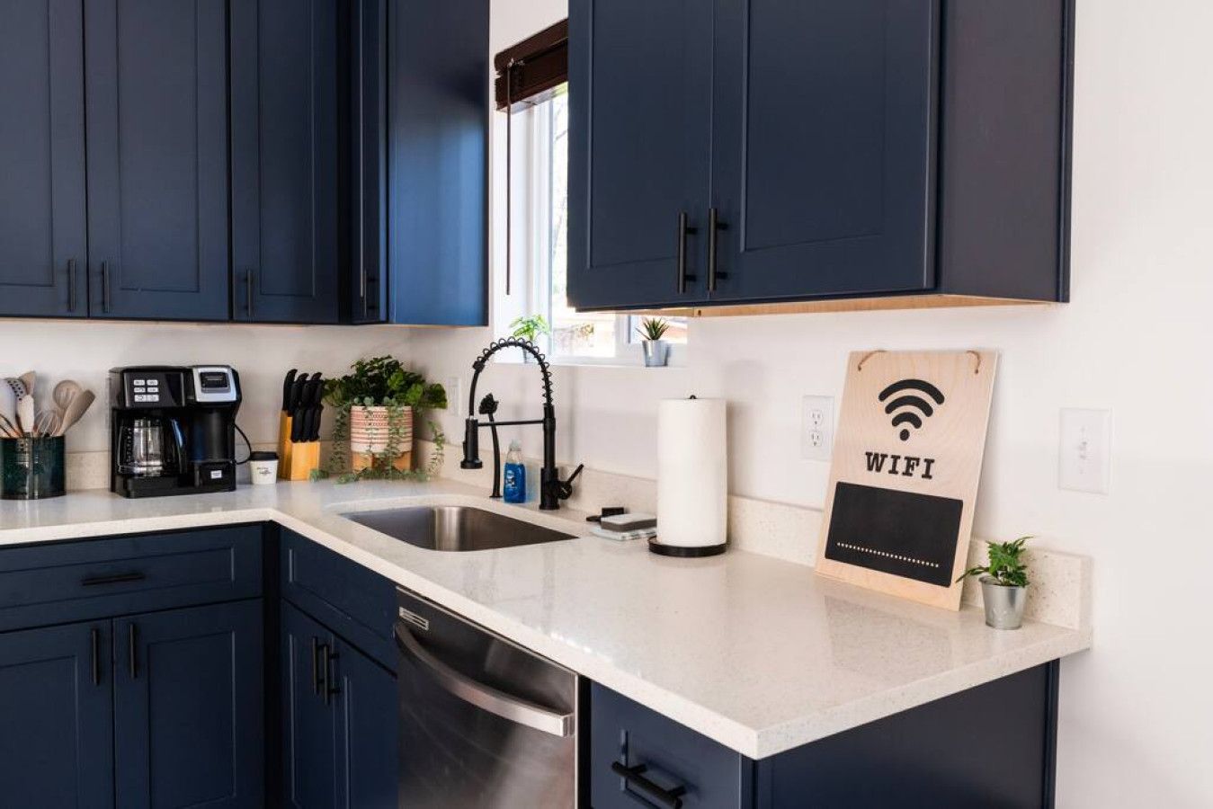 Une cuisine moderne avec des meubles de couleur sombre, un évier en acier inoxydable, une machine à café et un panneau indiquant la disponibilité du Wi-Fi.