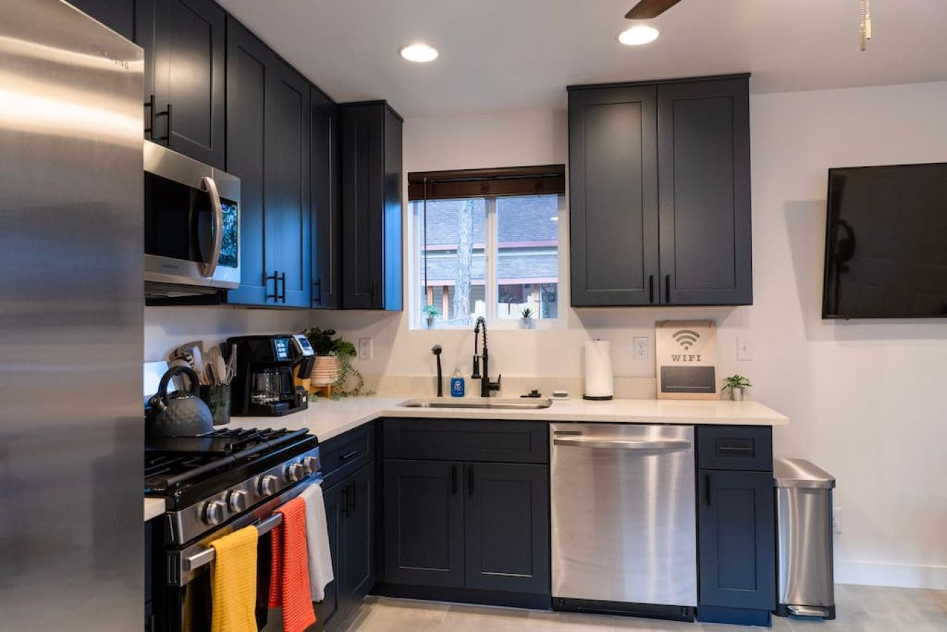 A modern kitchen with dark cabinets, stainless steel appliances, a window, and a WiFi sign.