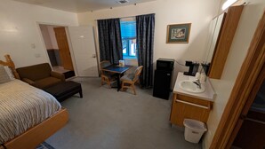 Une chambre d’hôtel comprenant un lit, un bureau, une chaise, une petite kitchenette et une salle de bain.