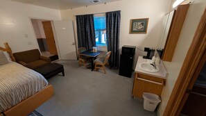 A hotel room with a bed, a desk, a chair, a small kitchenette, and a bathroom. - Home-like Cabin Room - Room 144 (Custer)