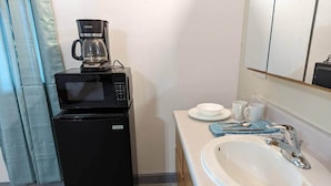 Une petite cuisine équipée d’une machine à café, d’un four à micro-ondes et d’un évier surmonté d’un miroir.
