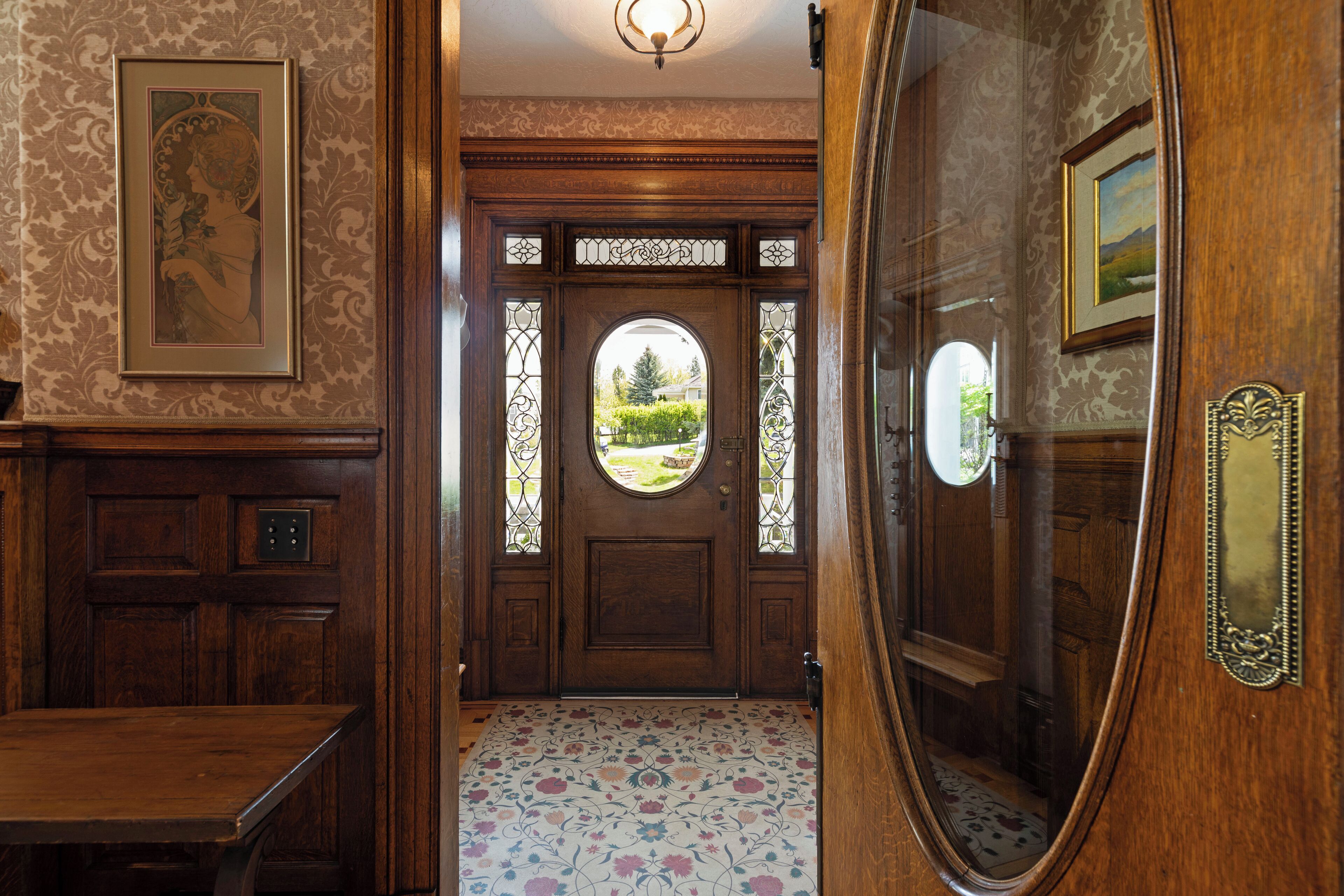 A wooden door with a circular window and decorative glass panels, leading to a room with patterned flooring and a wooden bench.