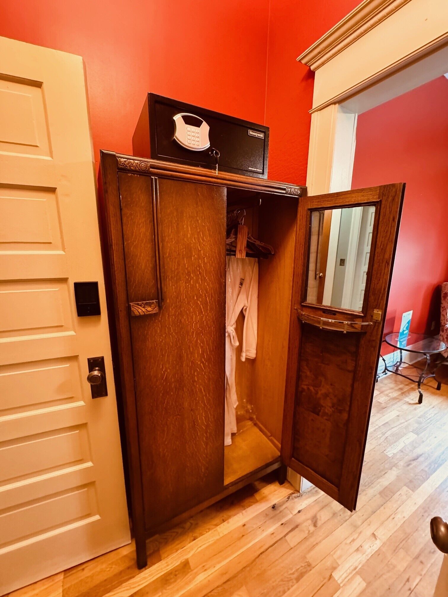 A wooden wardrobe with a mirror and a hanging robe, a white door, and a red wall.