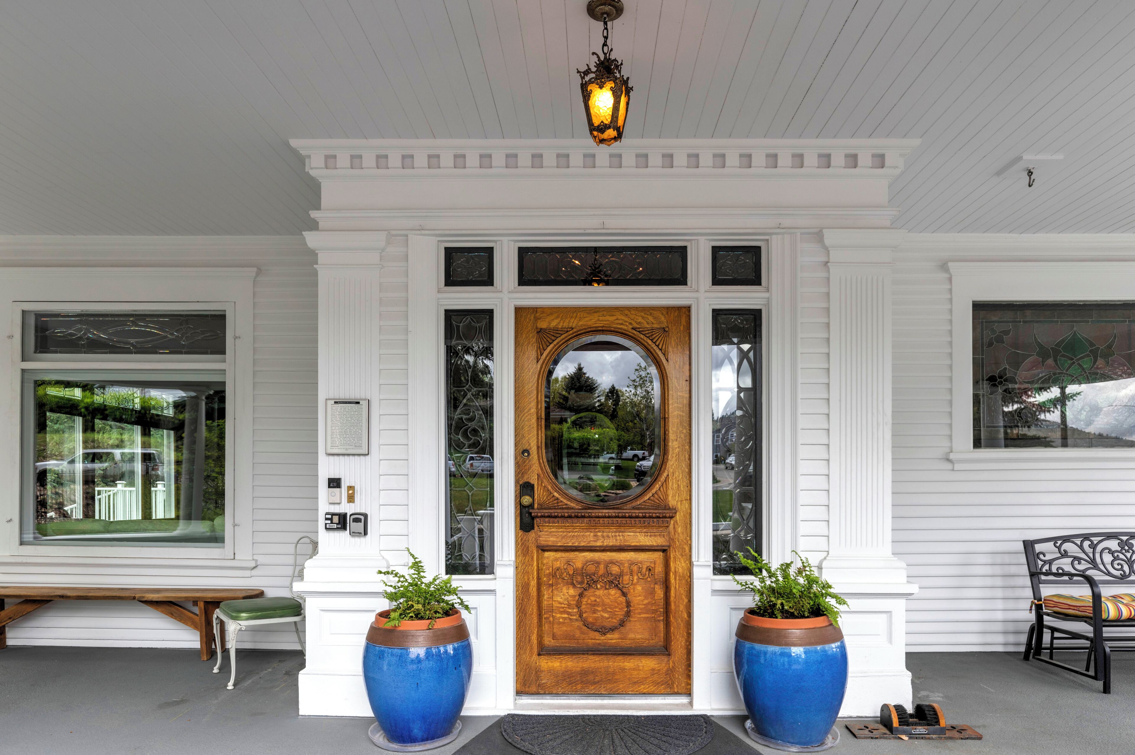 Een witte gevel met een houten voordeur, twee grote blauwe plantenbakken, een bank en een stoel.