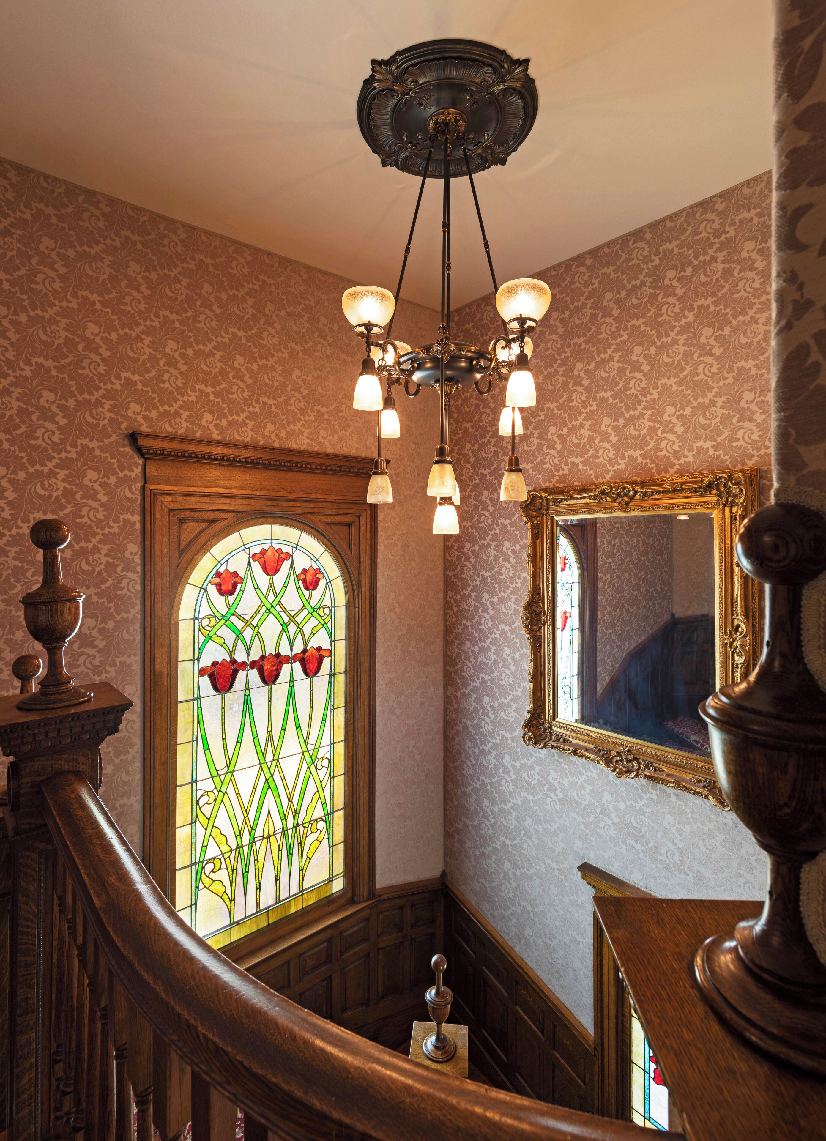 A grand staircase with a stained glass window and a chandelier.