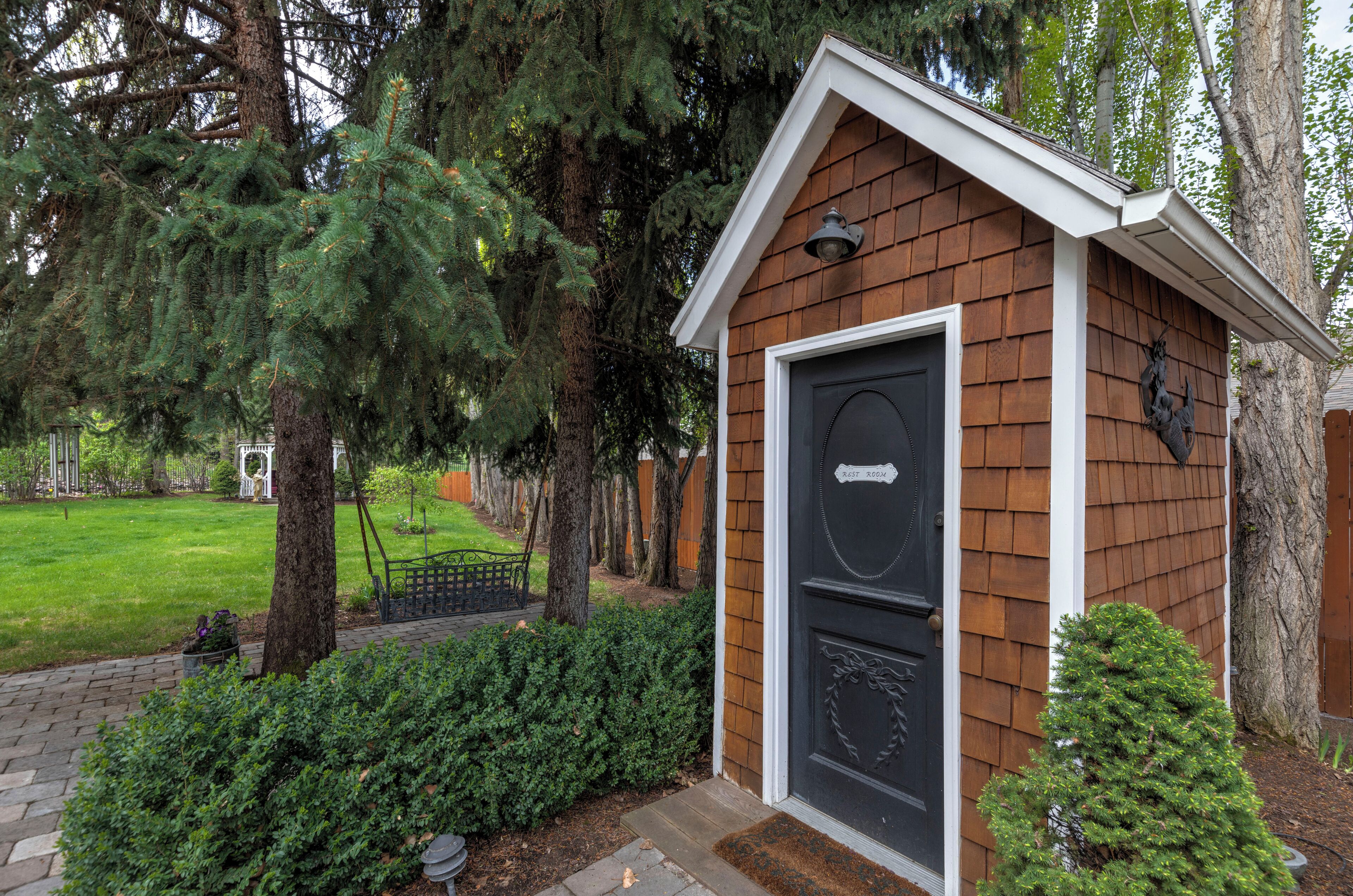 Une petite cabane en bois avec une porte noire, entourée d’arbres et d’une pelouse bien entretenue.