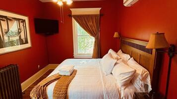 Un dormitorio con cama, ventilador de techo, ventana con cortinas, radiador, televisor y lámpara.