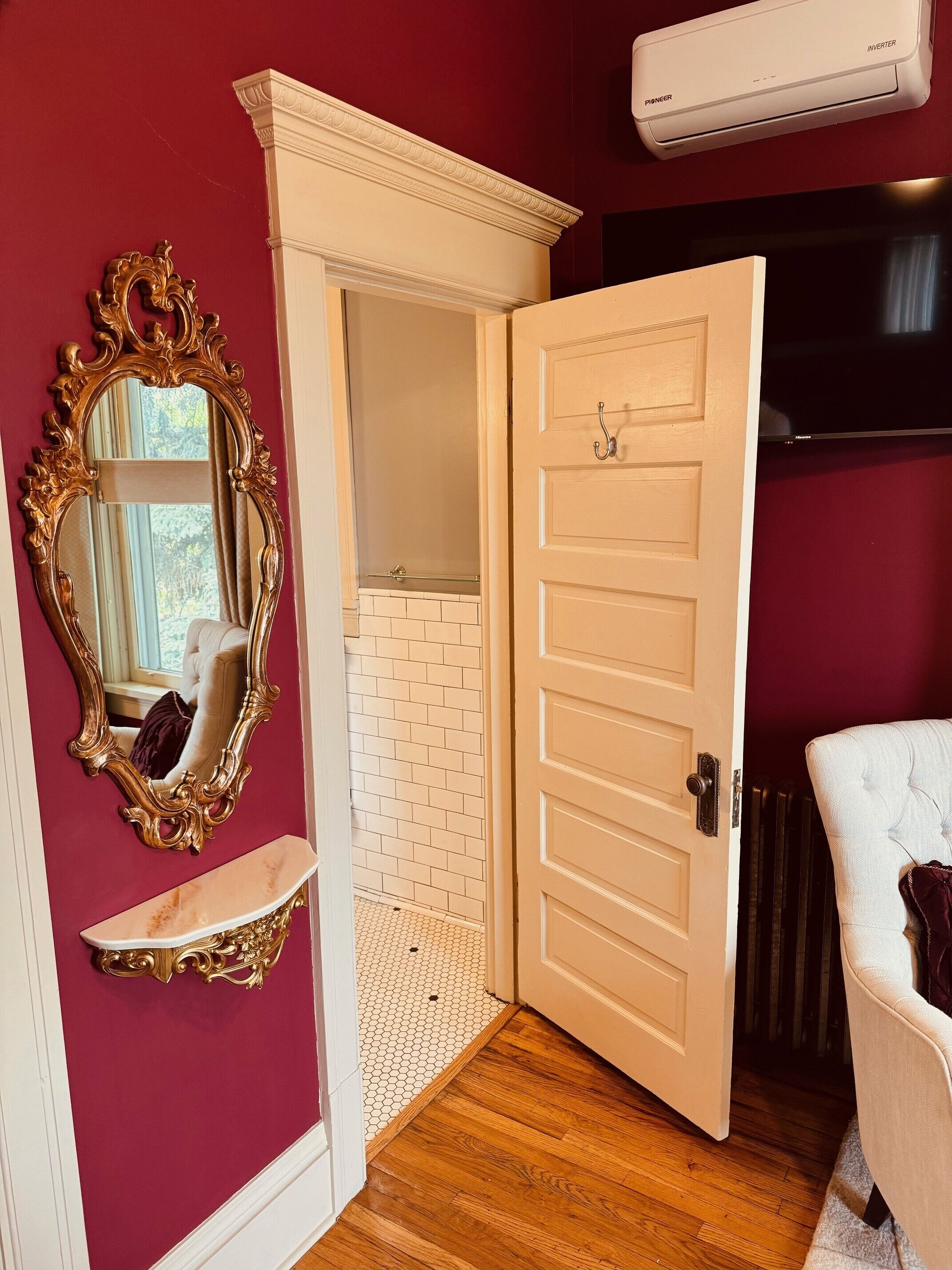 A room with a white door, a mirror with an ornate frame, a white brick wall, and a radiator.