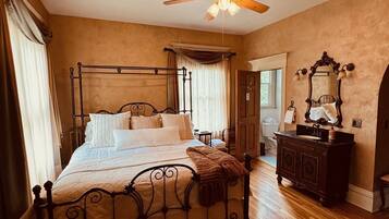 A bedroom with a four-poster bed, wooden flooring, a ceiling fan, and a vintage-style dresser.