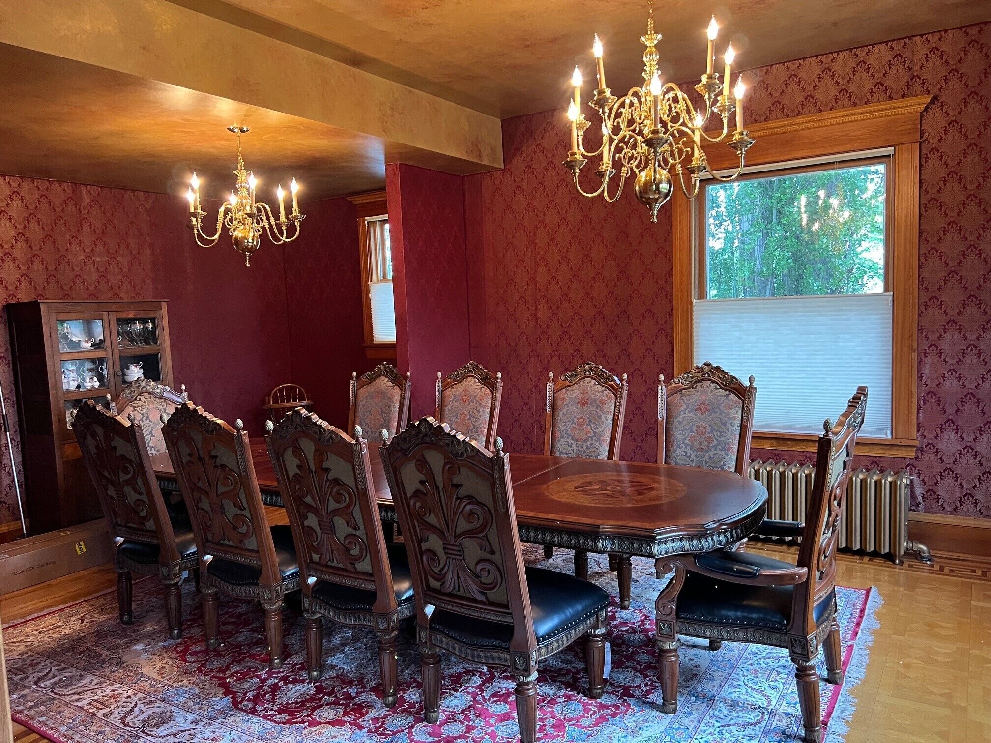 A dining room with a large wooden table, ornate chairs, a chandelier, and a view of trees through a window.