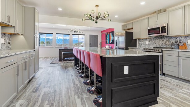 A modern kitchen with a central island, stainless steel appliances, and a view of mountains through large windows. - Interstellar Villa with 180° Mountain Range Views (Colorado Springs)