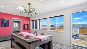 A dining area with a wooden table set for four, a pink table runner, and a view of mountains through large windows. - Interstellar Villa with 180° Mountain Range Views (Colorado Springs)