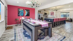 A modern kitchen with a central island, a dining area with pink chairs, and a bright red accent wall. - Interstellar Villa with 180° Mountain Range Views (Colorado Springs)