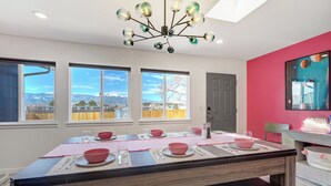 A dining area with a table set for four, large windows with a mountain view, and a modern chandelier. - Interstellar Villa with 180° Mountain Range Views (Colorado Springs)