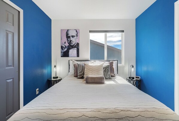 A hotel room with a bed, a window, and a painting on the wall.