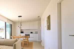 Eine moderne Küche mit weißen Schränken, ein Essbereich mit einem Holztisch und Stühlen, und ein großes Fenster mit Blick ins Freie.