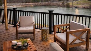 Eine Holzterrasse mit Gartenmöbeln, Blick auf einen Fluss und Lichterketten.
