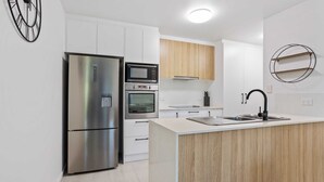 A modern kitchen with stainless steel appliances, wooden cabinets, and a central island. - Sunrise Cove (Mermaid Beach)