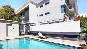 A modern building with a swimming pool, featuring a flat roof, large windows, and a balcony. - Sunrise Cove (Mermaid Beach)