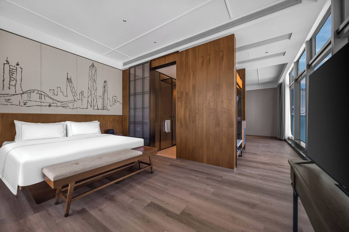 Une chambre d’hôtel moderne avec un grand lit, un plancher en bois, une fresque représentant un paysage urbain et un téléviseur.