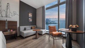 A modern hotel room with a large window offering a city view, a grey sofa, a wooden coffee table, and a small side table. - UrCove by Hyatt Shenzhen Shekou Cruise Center (Shenzhen)
