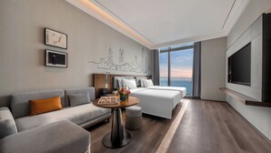 A modern hotel room with a sofa, a bed, a small table with a vase of flowers, and a large TV. - UrCove by Hyatt Shenzhen Shekou Cruise Center (Shenzhen)