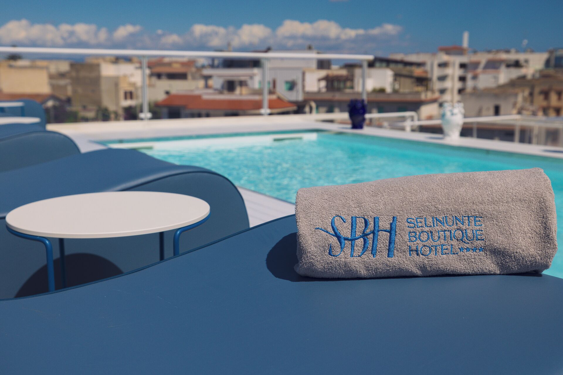 A poolside area with a towel labeled "SELINUNTE BOUTIQUE HOTEL" and a table.