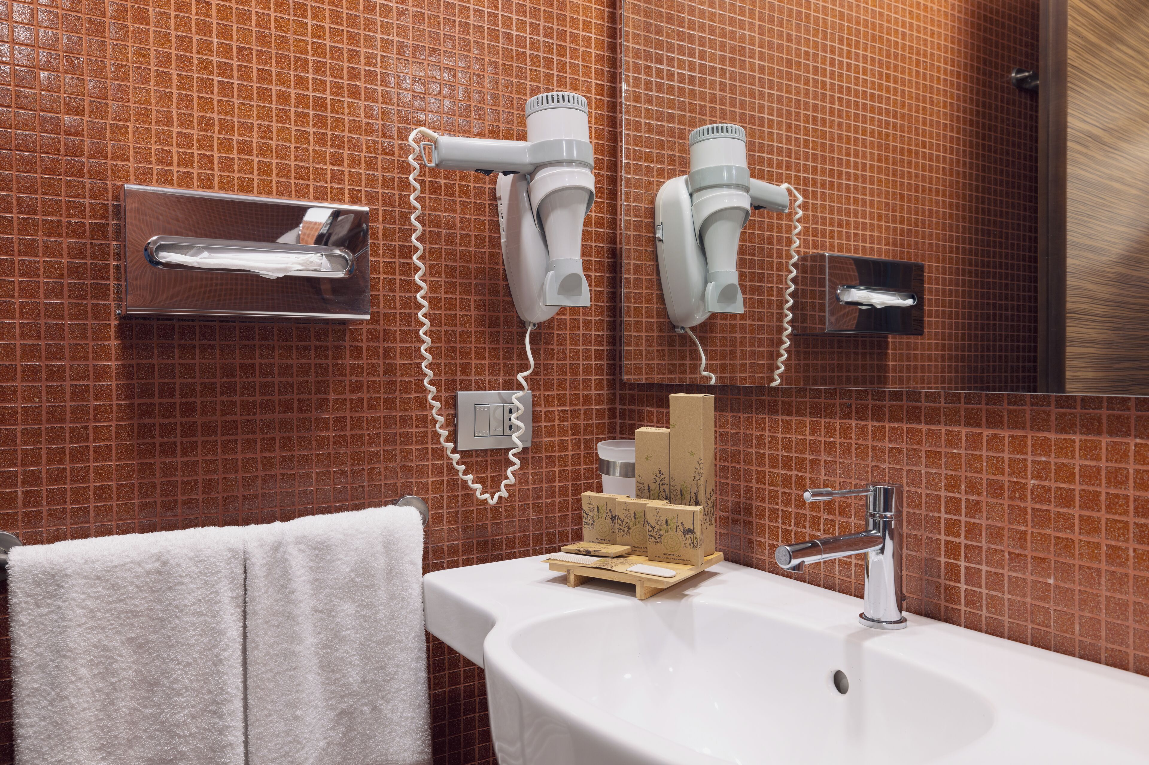 Une salle de bain avec un lavabo blanc, un miroir et deux sèche-cheveux fixés au mur.