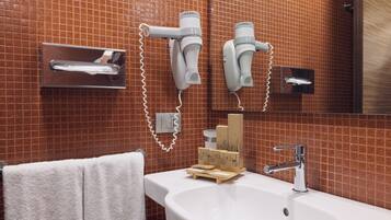 Une salle de bain avec un lavabo blanc, un miroir et deux sèche-cheveux fixés au mur.
