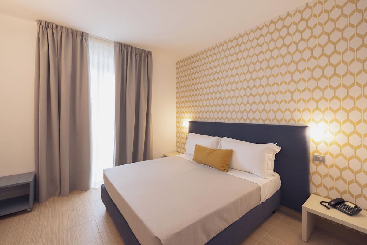 A hotel room with a bed, a nightstand, a telephone, and a window with curtains.