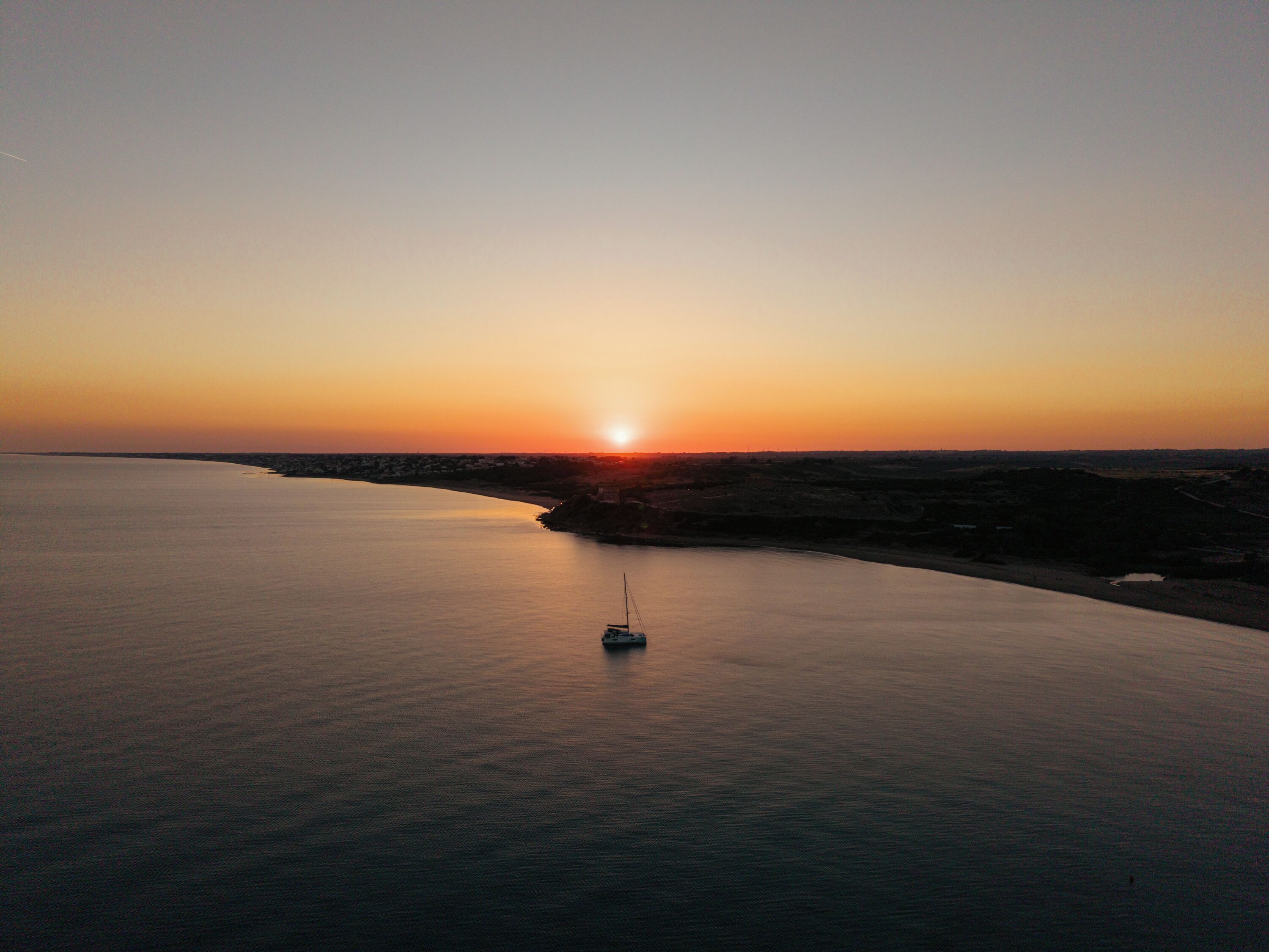 Une étendue d’eau calme, avec un seul bateau ancré au centre, entourée d’un paysage vallonné.