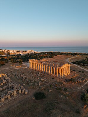 An ancient Greek temple with columns, surrounded by ruins and a coastal cityscape in the background. - Selinunte Boutique Hotel (Castelvetrano)