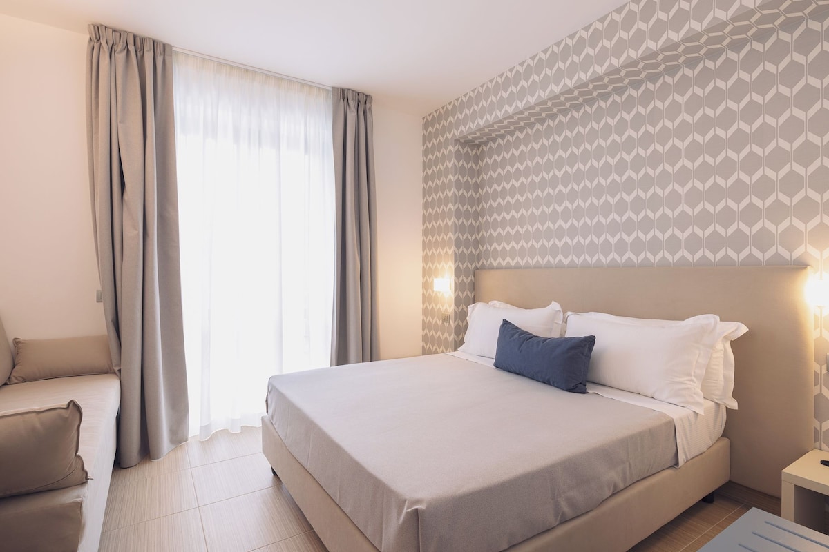 A hotel room with a bed, a sofa, a nightstand, and a patterned wall.