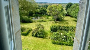Vista desde una ventana de un jardín con céspedes cuidados, árboles y un estanque.