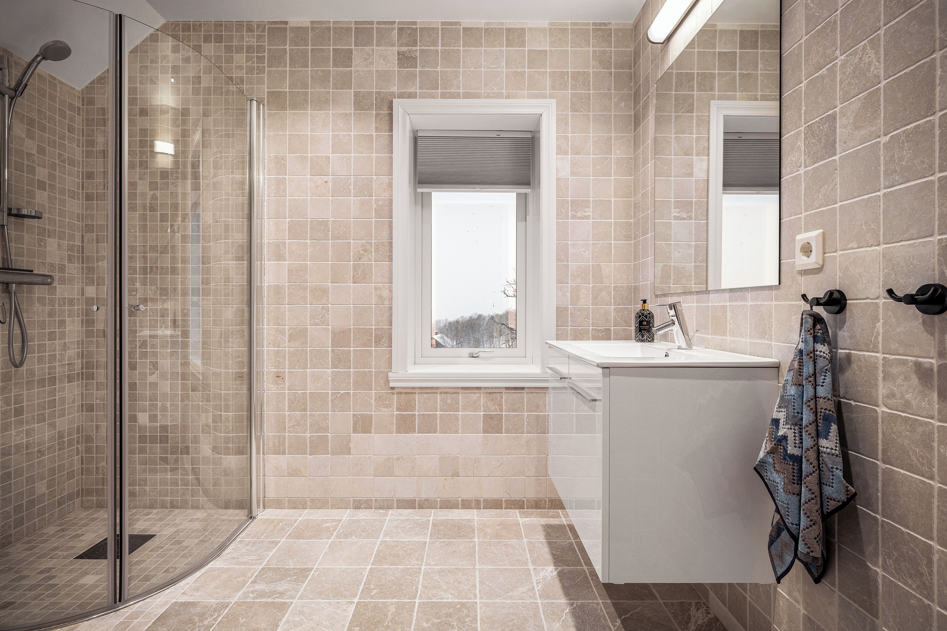 A modern bathroom with a glass shower enclosure, a window, and a white sink.