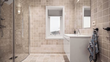 A modern bathroom with a glass shower enclosure, a window, and a white sink.