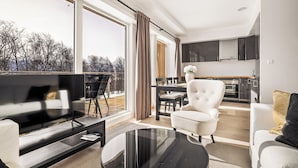 A modern living room with a flat-screen TV, a glass coffee table, and a dining area with a wooden table and chairs. - Gullstein (Hol)
