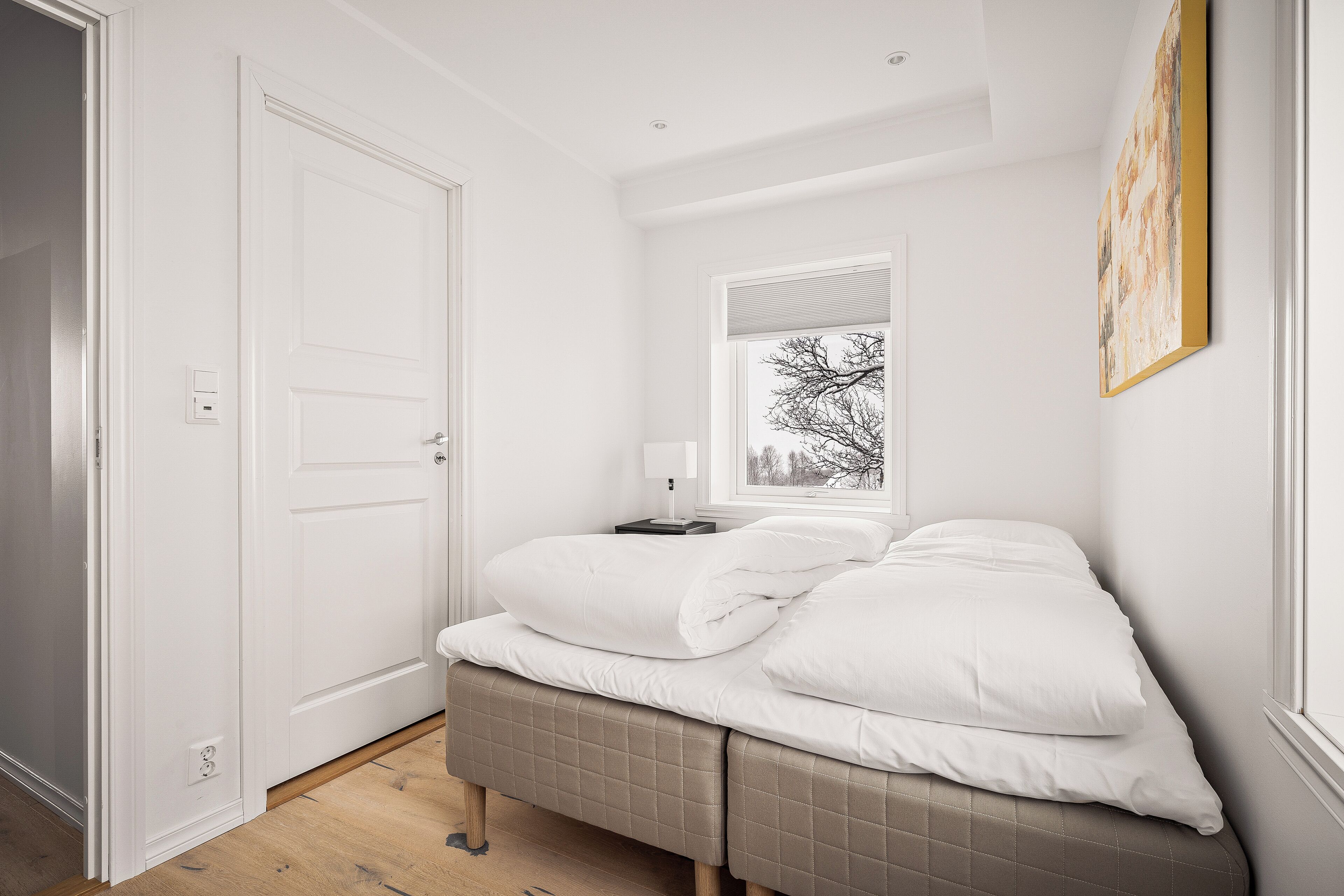 A bedroom with a bed, a bedside table, a window, and a door.