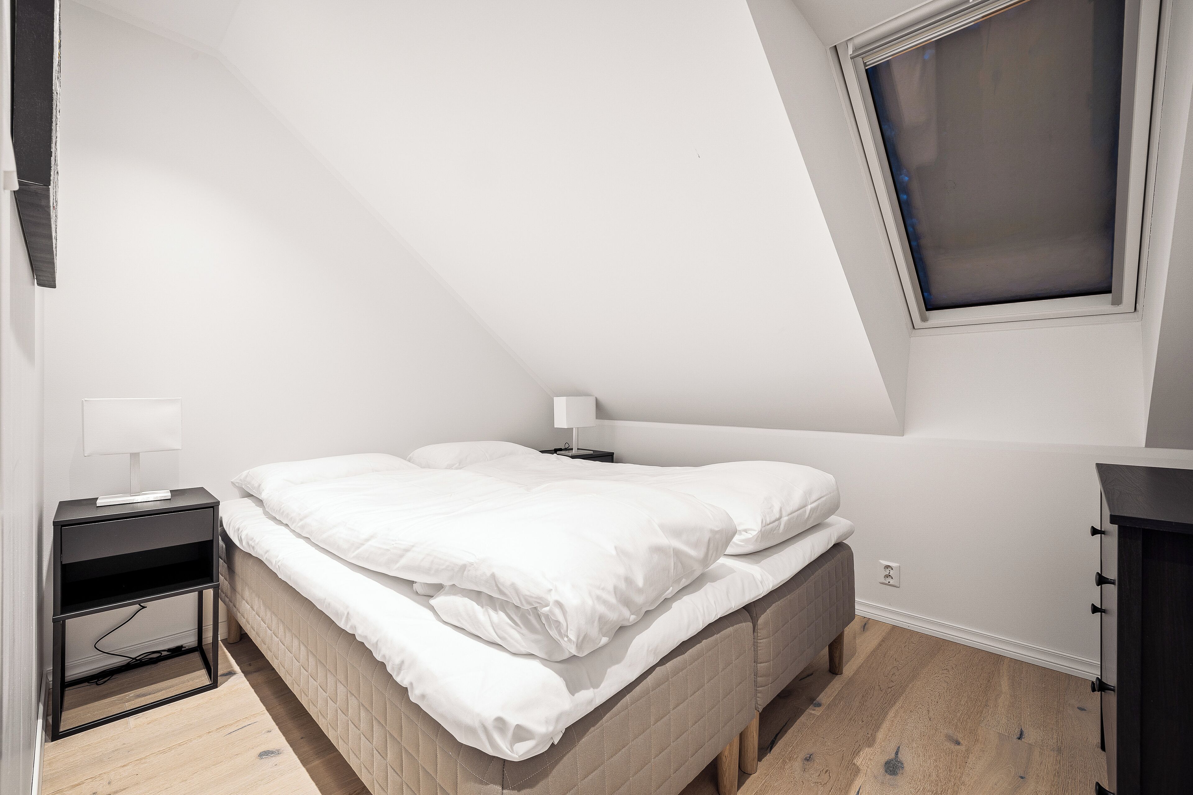 Un dormitorio con una cama, una mesita de noche, una lámpara y una ventana.