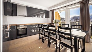 A modern kitchen with dark cabinets, a built-in oven, and a dining area with a wooden table and chairs. - Gullstein (Hol)