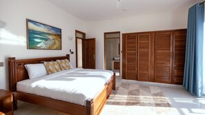 A bedroom with a bed, wooden wardrobe, and a painting on the wall. - Seaside Bliss Vipingo (Kilifi)