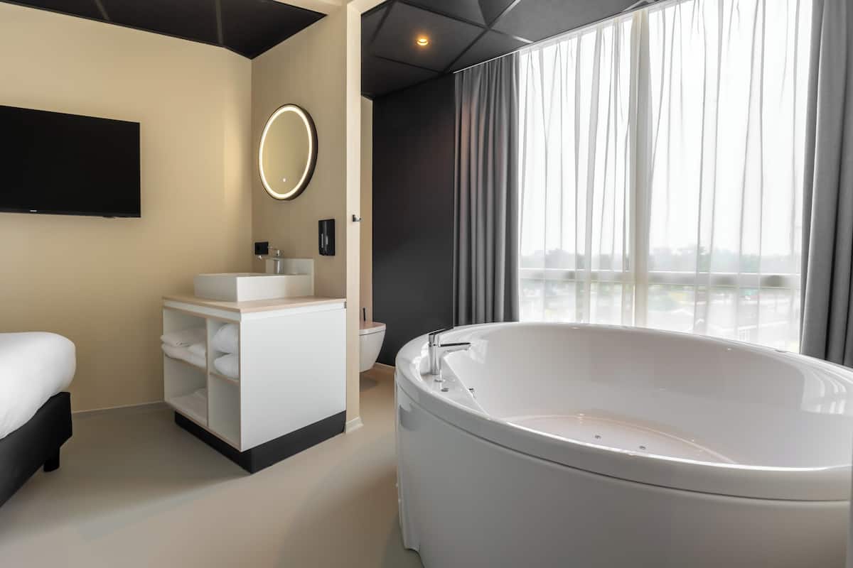 Ein modernes Hotelbad mit einer großen Badewanne, einem Waschtisch mit Spiegel und einer Toilette.