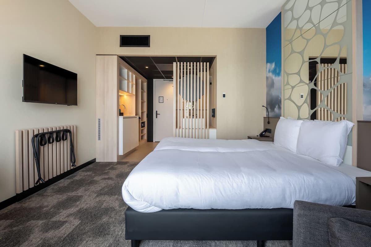 Ein Hotelzimmer mit einem großen Bett, einem an der Wand montierten Fernseher, einer Heizung und Blick ins Freie.