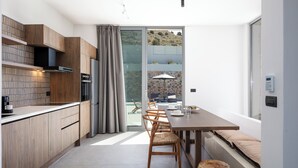 A modern kitchen with wooden cabinets, a dining area with a table and chairs, and a sliding glass door leading to a balcony with a view of a hillside. - Kōa Villa I, idyll Seaview Near Beach by etouri (Heraklion)