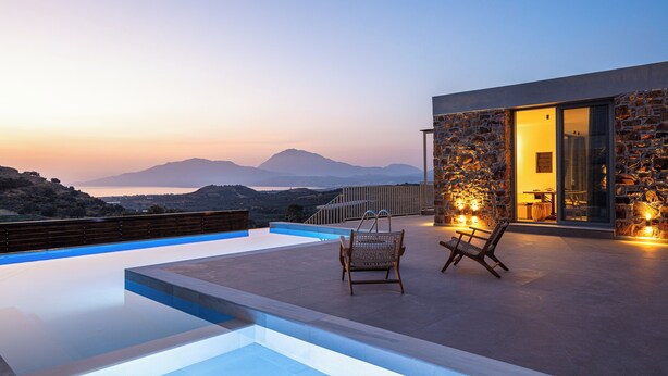A modern outdoor pool area with a stone wall, two wicker chairs, and a view of mountains at dusk. - Kōa Villa I, idyll Seaview Near Beach by etouri (Heraklion)